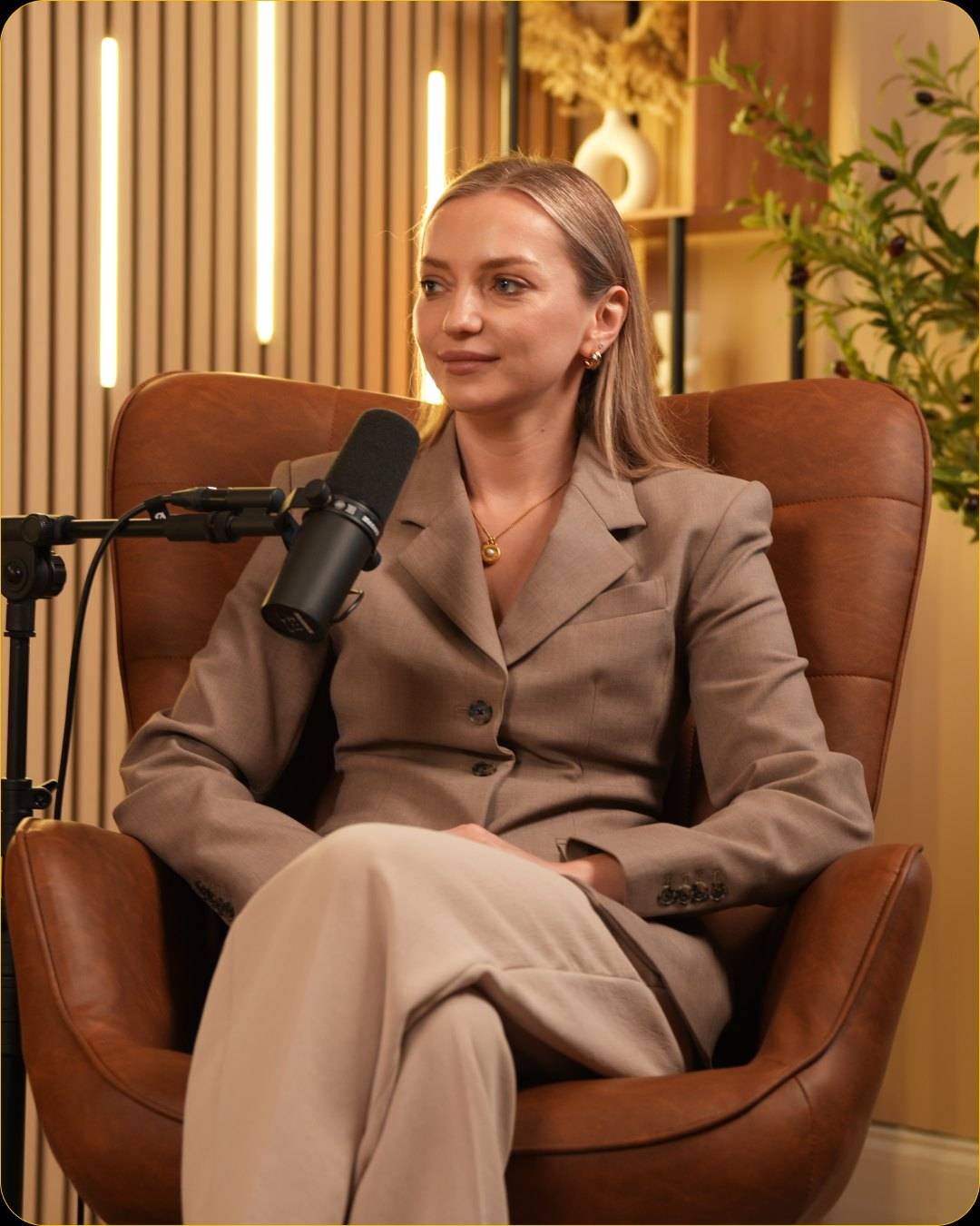 Studio #1 at The Cast Studio: A guest in a leather armchair at a microphone on a boom arm, with LED light bars on the wood panel wall behind.