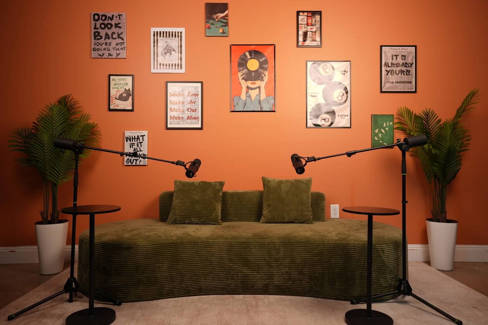 Studio #6 at The Cast Studio: The retro-pop set, with a green corduroy sofa in front of an orange gallery wall and a microphone on a boom stand on each side.