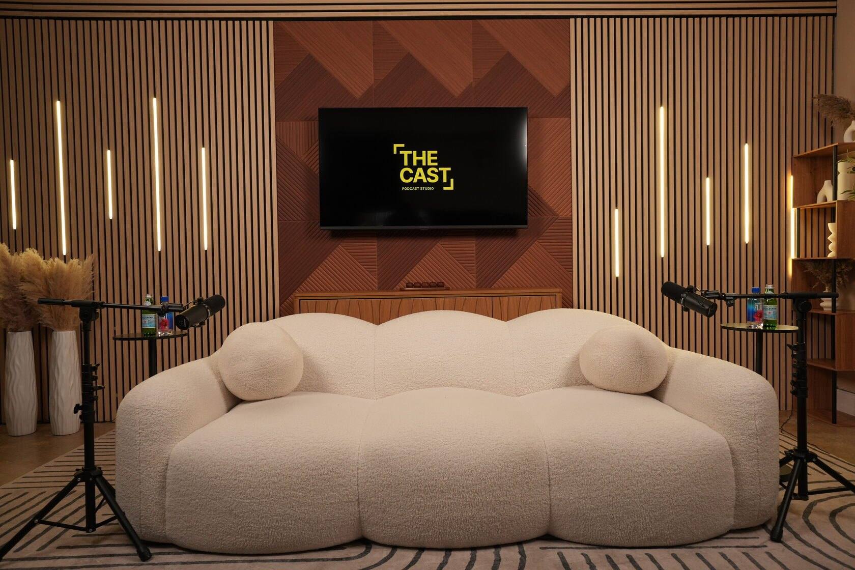 Studio #5 at The Cast Studio: a white sofa between two microphone stands in front of a wood panel wall with LED light bars