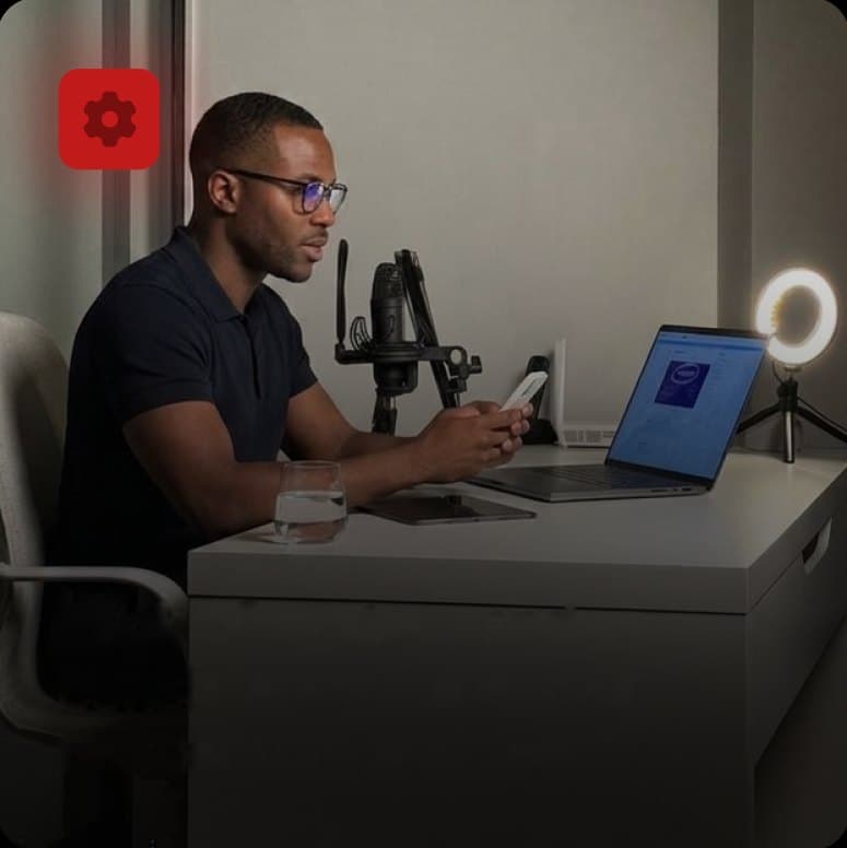 Man at a home desk setup with a microphone, laptop and ring light